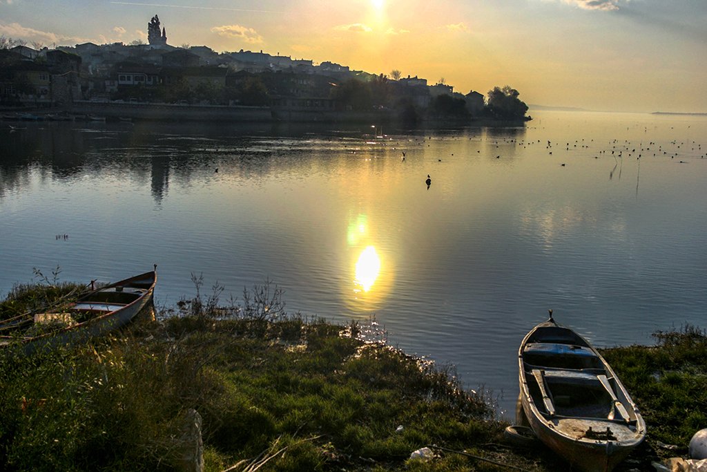 Uluabat Gölü'nde gün batımı, kıyıda balıkçı tekneleri ve arkada Gölyazı silueti